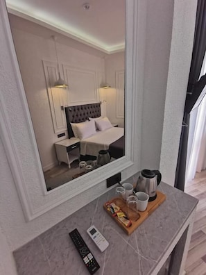 A hotel room with a large mirror, a bed with a tufted headboard, bedside tables, a wooden tray with cups and a kettle, and a remote control. - HOTEL EFZEN (Istanbul)