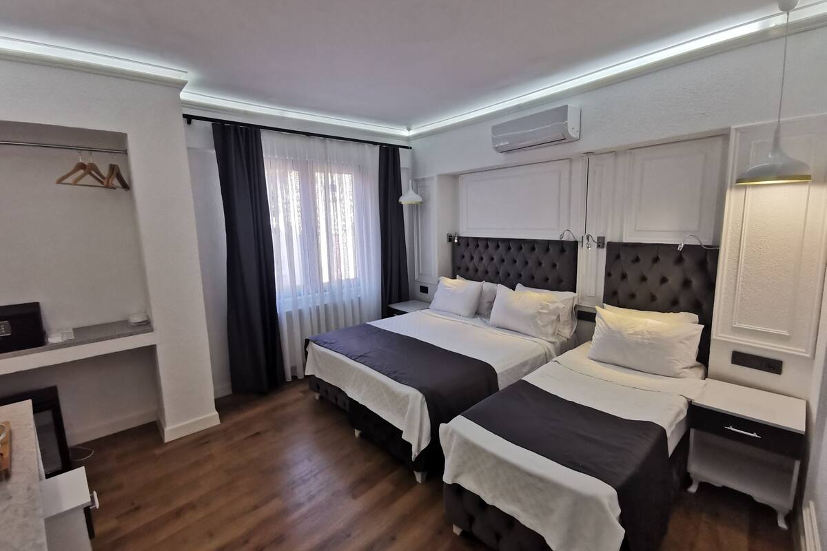 A hotel room with two beds, a wardrobe, a desk, and a window with curtains.