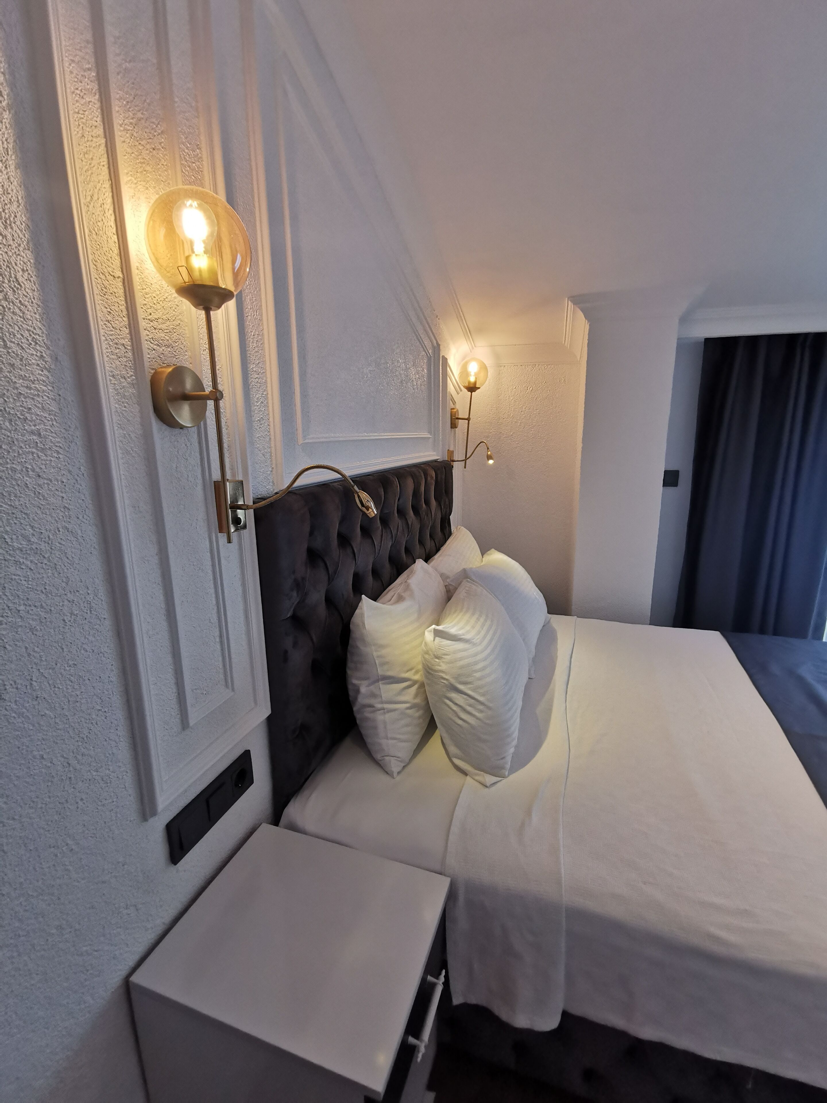 A bedroom with a tufted headboard, a bedside table, and two wall-mounted lamps.