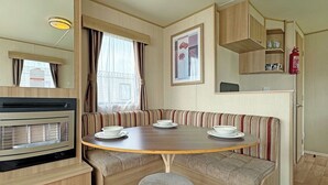 Un intérieur de camping-car compact comprenant une table à manger, des banquettes, un coin cuisine et une petite fenêtre.