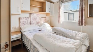 Dormitorio compacto en una autocaravana, con cama, un escritorio pequeño y una ventana con cortinas.