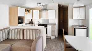 Un espacio habitable compacto con sofá, una mesa de comedor, kitchenette y un refrigerador pequeño.