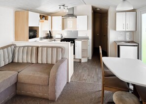Un espace de vie compact comprenant un canapé, une table à manger, un coin cuisine et un petit réfrigérateur.