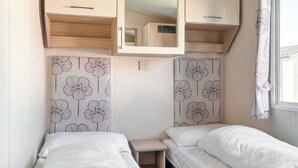 Un dormitorio pequeño con dos camas, armarios de madera y papel tapiz estampado con motivos florales.