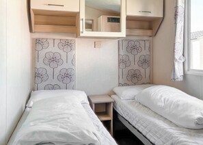 A compact bedroom with two beds, wooden cabinets, and floral-patterned wallpaper.