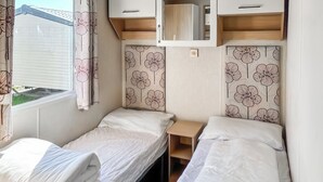 Un dormitorio de autocaravana compacto con dos camas, una mesita pequeña y una ventana con cortinas.