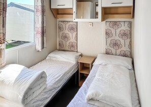 A compact RV bedroom with two beds, a small table, and a window with curtains.