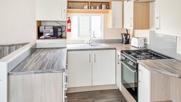 Una cocina moderna con armarios blancos, encimera de madera, estufa y pileta.
