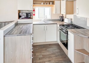 A modern kitchen with white cabinetry, a wooden countertop, a stove, and a sink.