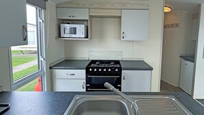 A compact kitchen with a stove, microwave, and cabinets. - Comfortable caravan with one double and one twin. (Mablethorpe, Skegness)