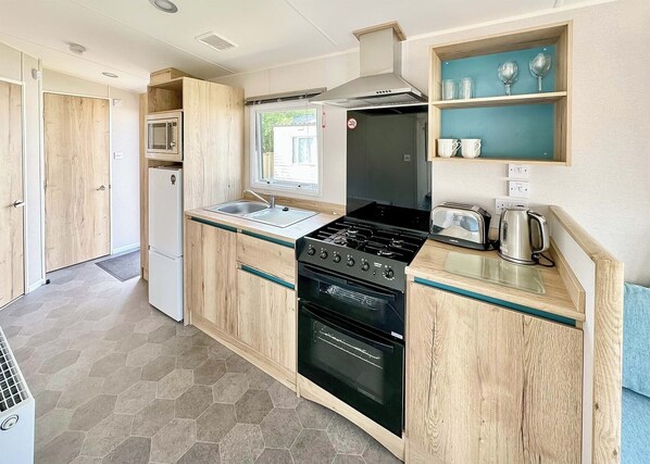 Een kleine keuken met een fornuis, oven, magnetron en een raam.