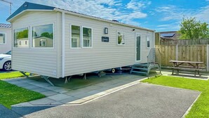 Une maison mobile dotée d’un patio couvert, d’une cour arrière clôturée et d’un panneau solaire sur le toit.