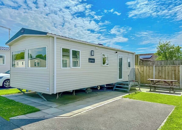 A mobile home with a covered patio, a fenced backyard, and a solar panel on the roof.