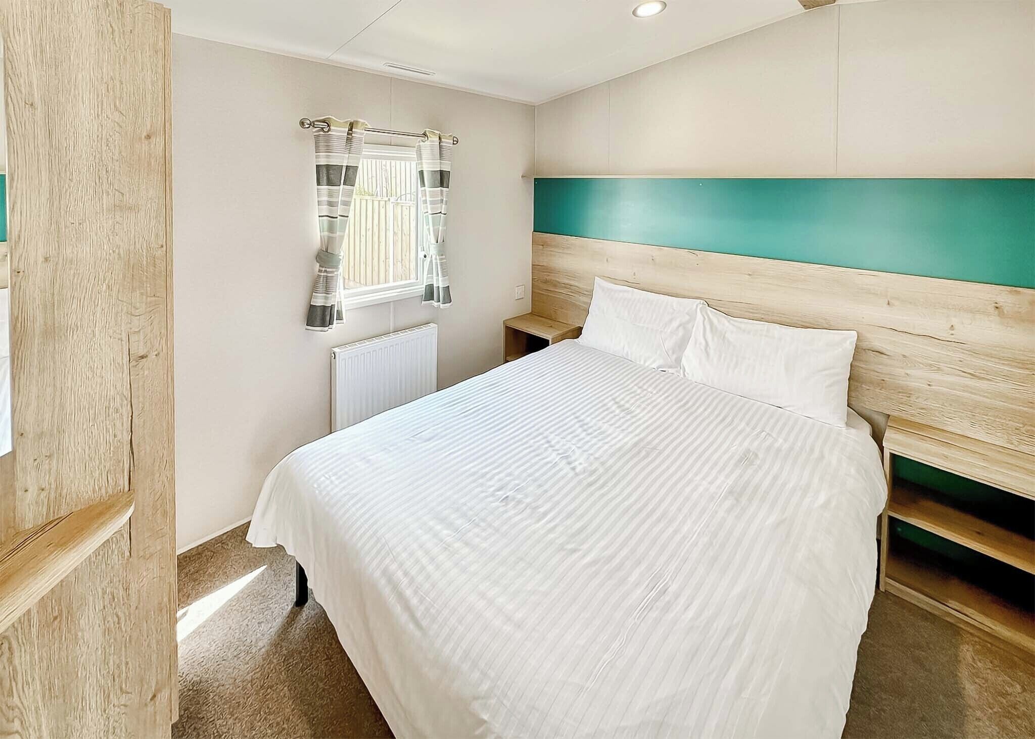 Une chambre à coucher avec un lit, une fenêtre avec des rideaux, un radiateur et une tête de lit en bois.