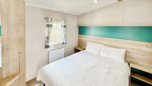 Une chambre à coucher avec un lit, une fenêtre avec des rideaux, un radiateur et une tête de lit en bois.