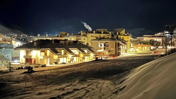 A snow-covered street with buildings, some with illuminated signs, and a clear sky. - First Tracks CB, Slopeside, true ski in/out above kids ski school! (Crested Butte)