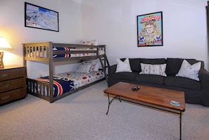 A bunk bed with a colorful bedspread, a sofa with patterned cushions, and a coffee table with a remote control. - First Tracks CB, Slopeside, true ski in/out above kids ski school! (Crested Butte)