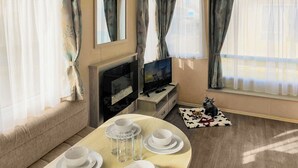 A furnished room with a sofa, a TV, a dining table set with plates and glasses, and a window with curtains.