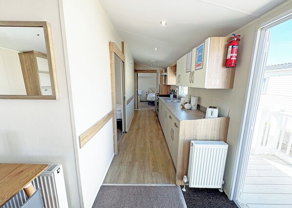 A narrow hallway leading to a kitchen with wooden cabinets, a radiator, and a fire extinguisher.