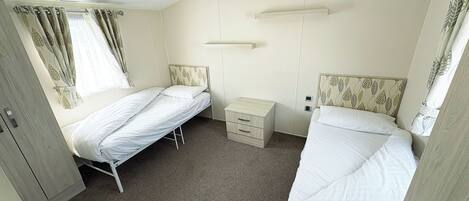Een kamer met twee eenpersoonsbedden, een klein nachtkastje, een kledingkast en een plafondlamp.