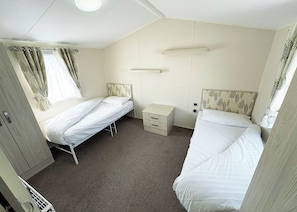 A room with two single beds, a small bedside table, a wardrobe, and a ceiling light fixture.
