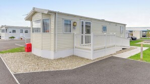 En etagers mobilbolig med en veranda, en lille tilhørende garage og en grusbelagt indkørsel.