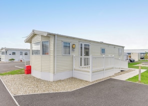 A single-story mobile home with a front porch, a small attached garage, and a gravel driveway.