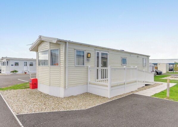 A single-story mobile home with a front porch, a small attached garage, and a gravel driveway.