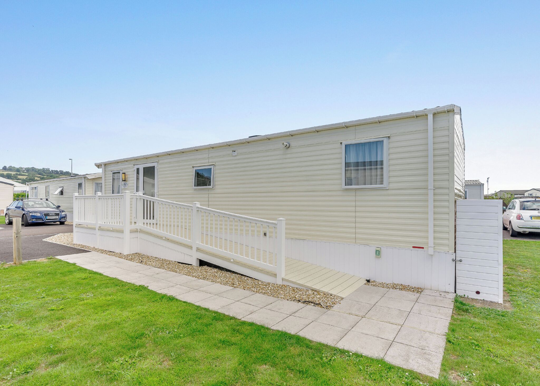 Une maison mobile de plain-pied, avec une façade blanche, un petit porche et une allée goudronnée.