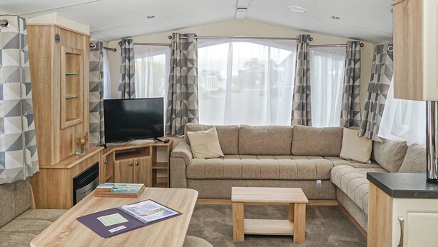 A compact RV interior with a sofa, a TV, a wooden table, and a kitchenette. - 2 bedroom accommodation in Gwespyr, Nr Prestatyn, Denbighshire (Gwespyr, Nr Prestatyn, Denbighshire)