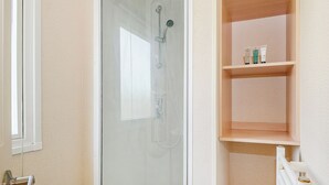 Een badkamer met een glazen douchecabine, een houten plank met toiletartikelen en een witte handdoekradiator.