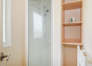 A bathroom with a glass-enclosed shower, a wooden shelf with toiletries, and a white radiator.