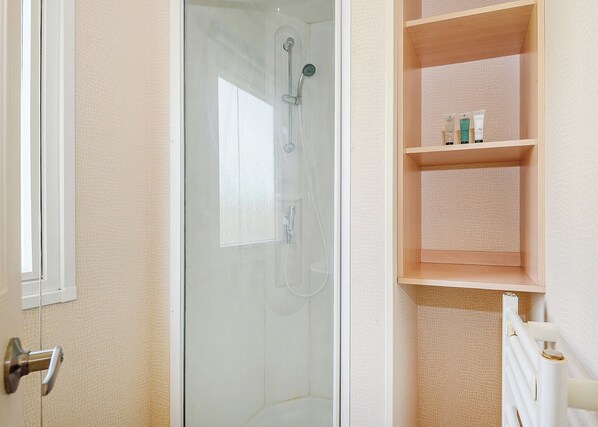 Une salle de bain avec une douche à parois de verre, une étagère en bois où sont rangés les articles de toilette et un radiateur blanc.