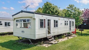 Een gelijkvloerse stacaravan met een voortuin, een kleine aangebouwde garage en een zichtbare boiler.