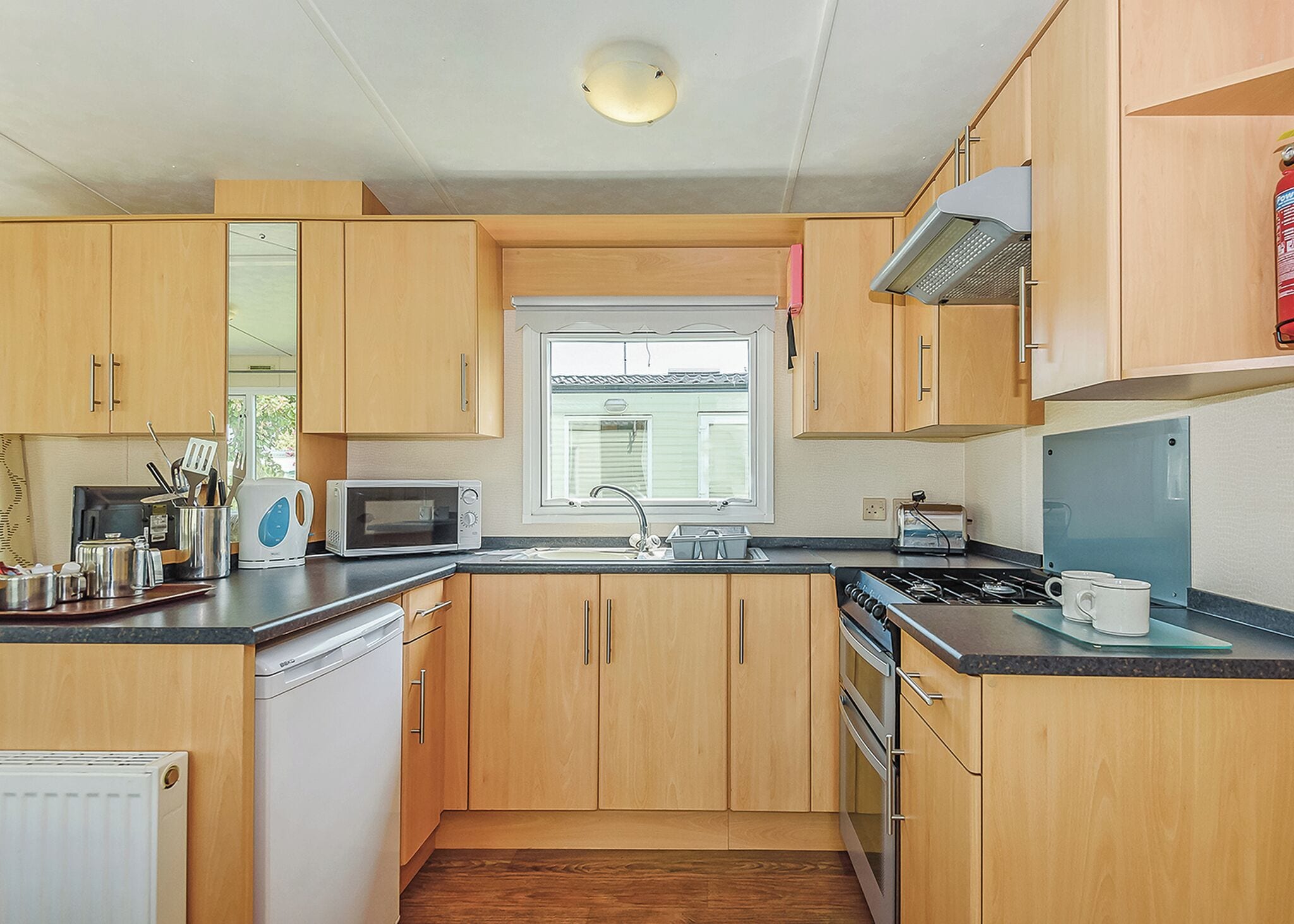 A compact kitchen with wooden cabinets, a microwave, a stove, and a window.