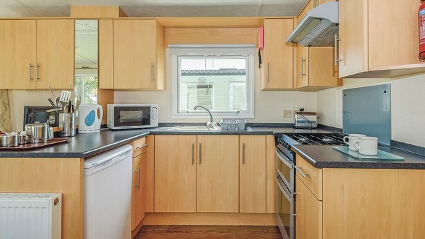 Een kleine keuken met houten kastjes, een magnetron, een fornuis en een raam.