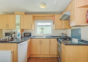 A compact kitchen with wooden cabinets, a microwave, a stove, and a window.