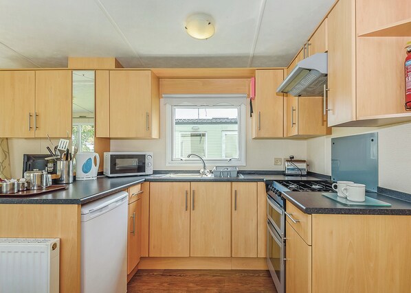 Una cocina compacta con armarios de madera, un microondas, una estufa y una ventana.