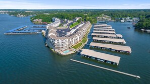 A waterfront hotel with multiple docked boats, a central building with balconies, and a marina. - Ledges Landing – Waterfront Condo, Beach, & Pools! (Osage Beach)