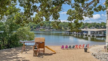 A sandy beach with a wooden play structure, a slide, and colorful chairs.