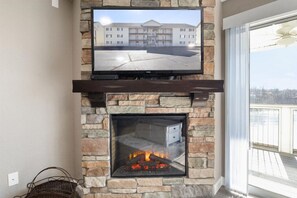 A stone fireplace with a TV mounted above it, a wicker basket, and a view of a building through the glass door.