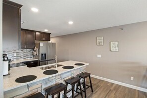 A modern kitchen with a central island, bar stools, and a refrigerator.