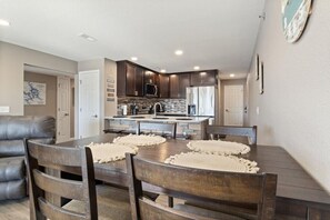 A modern kitchen with dark wood cabinets, a central island, and a dining area with a wooden table and chairs. - Ledges Landing – Waterfront Condo, Beach, & Pools! (Osage Beach)