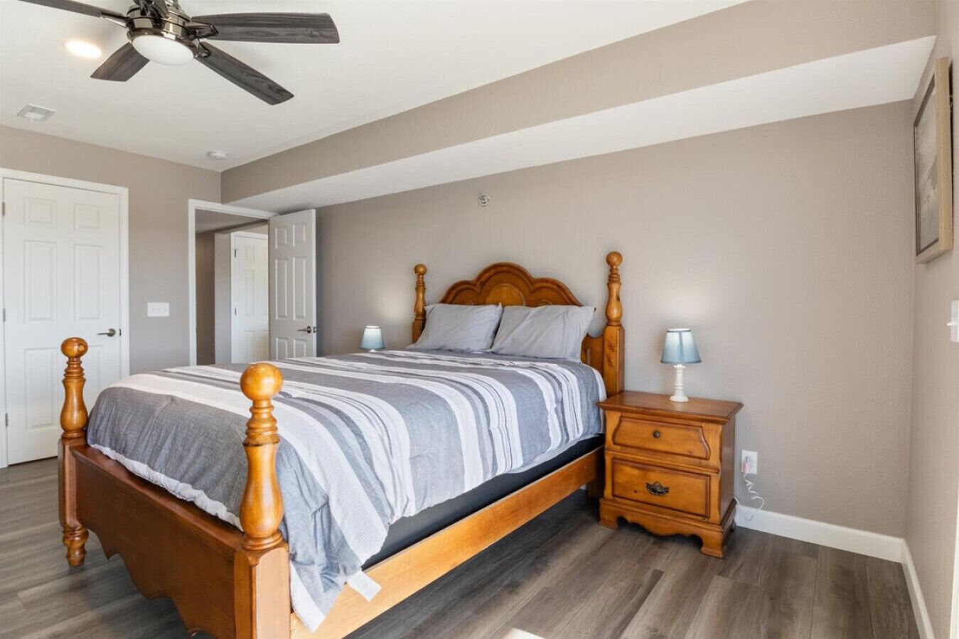 A bedroom with a wooden bed, bedside tables, a ceiling fan, and a door.