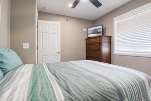 A bedroom with a bed, a dresser, a door, and a window with blinds.