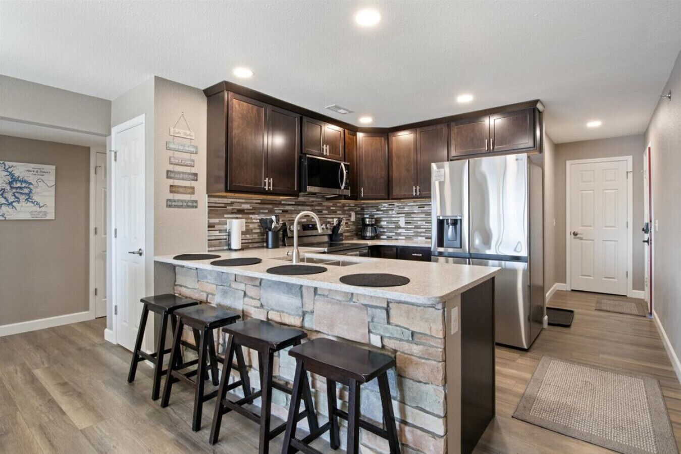 Cocina moderna con alacenas de madera oscura, una isla central con taburetes, un refrigerador de acero inoxidable y un microondas.