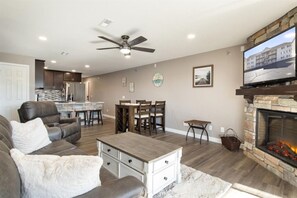 A modern living room with a fireplace, a dining area, and a kitchen in the background. - Ledges Landing – Waterfront Condo, Beach, & Pools! (Osage Beach)