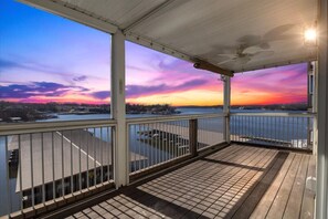 A covered outdoor deck with a view of a sunset over a body of water.