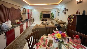 Un salon moderne avec un canapé, une table à manger agrémentée de centres de table floraux et un coin cuisine équipé de placards et d’un réfrigérateur.