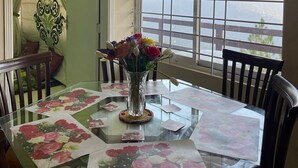 Un coin repas avec une table en verre, des sets de table à motifs floraux et un vase rempli de fleurs.